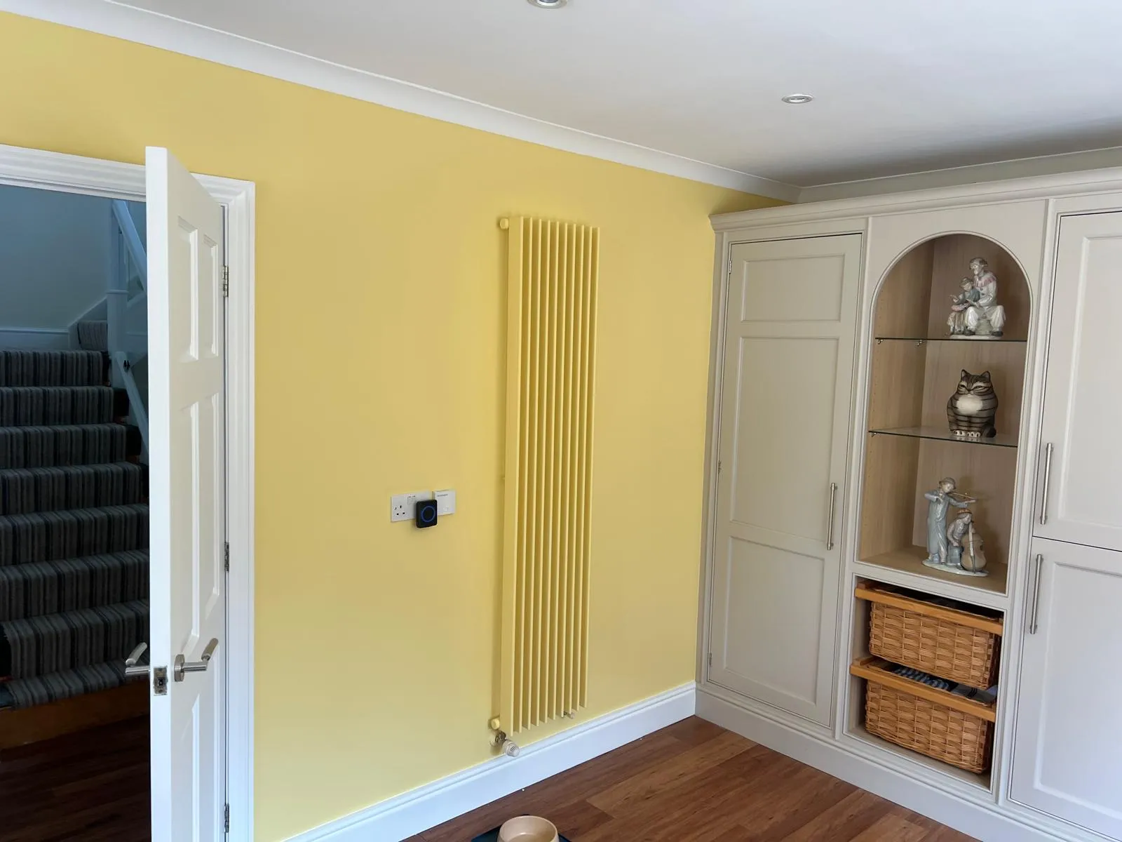 Hallway with yellow walls, a tall radiator and painted fitted cupboards